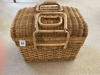 Closed wicker picnic basket with handle and two latches on the front.