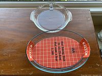 Clear glass Anker Hocking pie plate and Pyrex 3L oval bake dish on wooden table, both clean and intact.