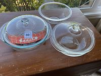 Clear glass Pyrex bowls with two glass lids on wooden surface near window showing all items together