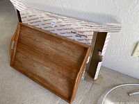 Handcrafted teak tray placed upright against a box with Upper Teakwood branding, showing natural teak grain and handles on sides.