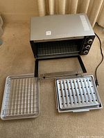 Photo of the Hamilton Beach toaster oven with the door open, showing two metal trays placed on the floor in front of it.