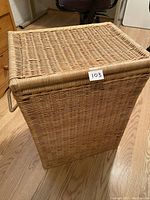 Closed wicker laundry basket, rectangular shape, natural color, with side rope handles.