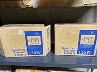 Two boxed new wooden foot stools on a shelf.