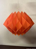 Front view of the orange butterfly pendant lamp hanging against a white textured wall.