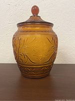 Front view of the amber glass cookie jar showing floral and leaf embossed design with round knob lid.