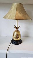Photo showing the full brass pineapple table lamp with beige fabric shade, black base, and power cord.