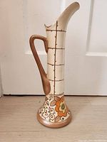 Front angle of tall pottery vase showing handle, narrow neck, and decorated base with floral patterns