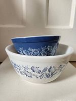 Two stacked Colonial Mist mixing bowls, white larger bowl with blue floral design and smaller blue bowl with white floral design on side.