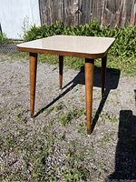 Full view of the side table showing thick square cream-colored arborite top with gold flecks and four tapered wooden legs with metal tips
