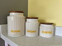 Front view of all three canisters labeled Flour, Sugar, Coffee with wooden lids.