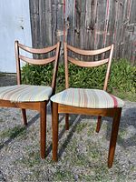 Front angled view of two mid-century dining chairs showing walnut wooden frames and striped upholstered seats.