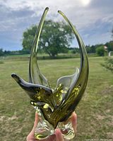 Front perspective showing the full height and organic form of the avocado green Murano style glass dish, held against an outdoor background.