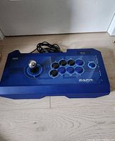 Top view of the blue Hori RAP4 arcade stick with joystick and blue and black buttons arranged on the faceplate. Shows USB cable and button layout.
