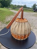 Full view of teak pendant light showing pleated beige and orange fabric shade and teak arm resting on a black table outdoors.