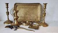 Full assortment view of the vintage brass items: two candlesticks, large etched tray, ashtrays, candle snuffer, small candlestick, and brass lizard figurine.