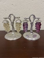 Pair of metal stands holding grape-shaped salt and pepper shakers in purple and yellow glass, showing overall vintage condition and design details.