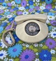 Overall view of the beige vintage rotary phone with coiled cord on floral fabric background.