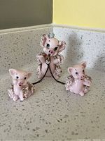 Full shot of the vintage spaghetti pig family showing parent pig with two piglets connected by metal chains on a speckled countertop with yellow and grey walls in background.