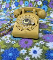Front view of yellow Northern Electric rotary dial phone on floral fabric background.