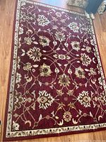 Full view of the burgundy area rug with a cream and beige floral pattern laid out on a wooden floor.