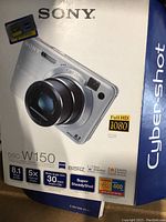 Photo of the camera box showing Sony Cyber-shot branding, specs such as 8.1 megapixels, 5x optical zoom, Super SteadyShot, and Full HD 1080 video capability.