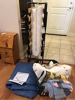 Folded metal frame day cot with mattress hanging, basket with bedding and knit items on floor, blue single bedspread below.