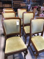 Set of six wood dining chairs with sage green upholstery shown from front and side angles in a warehouse setting.