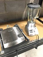 Photo showing the Breville sandwich grill press on the left and Black & Decker blender on the right on a wooden surface.