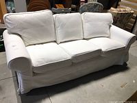Front view of white three seater sofa with three loose seat and back cushions covered in slipcover.