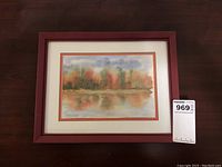 Full view of the framed watercolor showing the colorful tree-lined water landscape with matting and reddish frame.