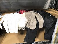 Photo shows laid out clothing including a white knit sweater, beige knit cardigan, black snow pants, and scarves.