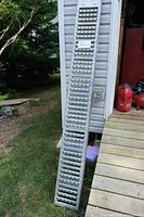 Full view of one aluminum loading ramp leaning against house wall, showing perforated tread surface and length approx. 8 feet.