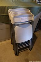 Photo of stacked 8 white folding chairs with gray metal frames showing front and side view.