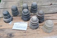 Eight insulators displayed on a wooden surface, including five Hemingray-marked pieces and three unidentified. Various shapes, primarily dark colors with some lighter and clear pieces, showing weathered condition.
