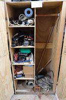 Full view of wooden cabinet with four shelves and a larger empty compartment. Shelves contain various tools and accessories including hoses, gauges, clamps, and boxes.
