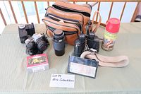 Full spread of lot contents on table including camera, binoculars, thermos, leather case, cards, and boxed toy.