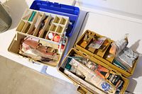 Two full tackle boxes containing various fishing lures, hooks, and tackle supplies including a brass scale.