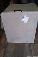 Photo of the folding table folded in half showing the plastic surface with a handle and a taped label with the dimensions 64x28.