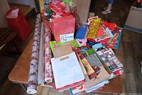 Photo showing assorted gift wrap rolls and a large assortment of colorful gift bags on a table.