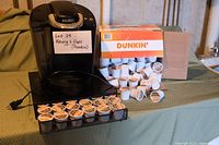 Black Keurig coffee maker next to cardboard box with many Dunkin' branded K-Cups spilled out and arranged.