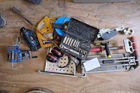 Overview of tools and accessories laid on wooden floor including socket set, measuring reels, ear muffs, clamp, pulley, and other hand tools.