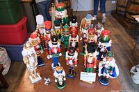 Group photo showing 17 wooden nutcracker figurines arranged in rows on the floor. Various sizes and colorful costumes with detailed facial expressions.