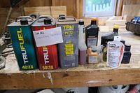 Photo shows multiple cans of small engine gas mixture and various bottles of 2-cycle engine oil and related fluids on a workbench.