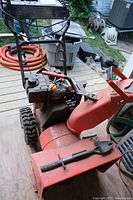 Red single-stage snow blower with visible engine and handle controls from front and side angles
