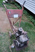 Full view of a gas-powered tiller with a red frame, black engine, two wheels, and tilling blades.