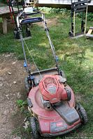 Photo of the full Toro lawn mower from a front angle showing the red body, handlebar, and wheels on grass.