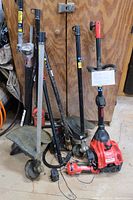 Photo showing assembled weed wacker and multiple attachments including shaft extensions and heads with guards, leaning against wooden surface.