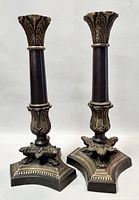 Front view of two cast bronze candleholders with claw feet, showing detailed leaf patterns on top and hexagonal bases with claw feet.