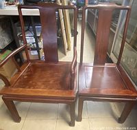 Two wooden chairs, one armchair and one side chair, shown from front angle on floor