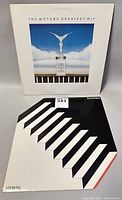 Two vinyl record albums by The Motors. Front shows The Motors Greatest Hit album with white cover and silver statue on column. Back shows second album with black and white stair-step geometric design.